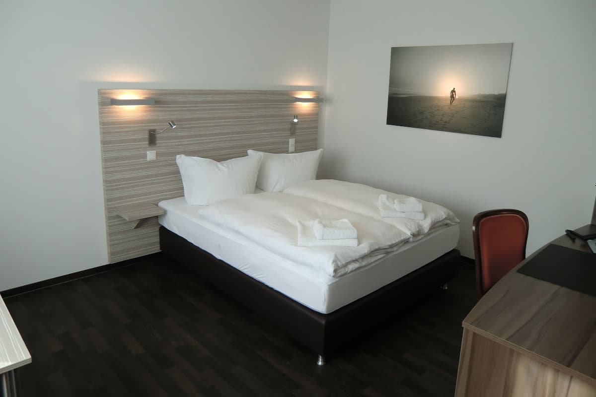 A modern hotel room with a large bed, a desk, and a chair.