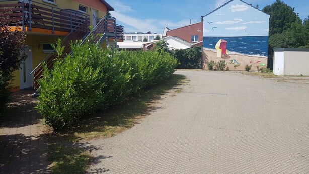 A paved pathway leading to a building with a red roof and a mural of a beach scene. - Apartment-Vermietung Brunner (Rostock)