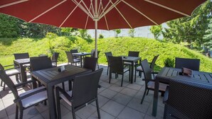 Un patio al aire libre con mobiliario de mimbre y un gran paraguas rojo.