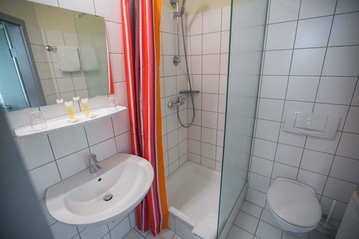 Un baño con un lavabo blanco, un espejo, una ducha con puerta de cristal y un inodoro.