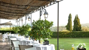 Un área de comedor al aire libre con mesas dispuestas para una comida, rodeada de vegetación y vistas al campo.