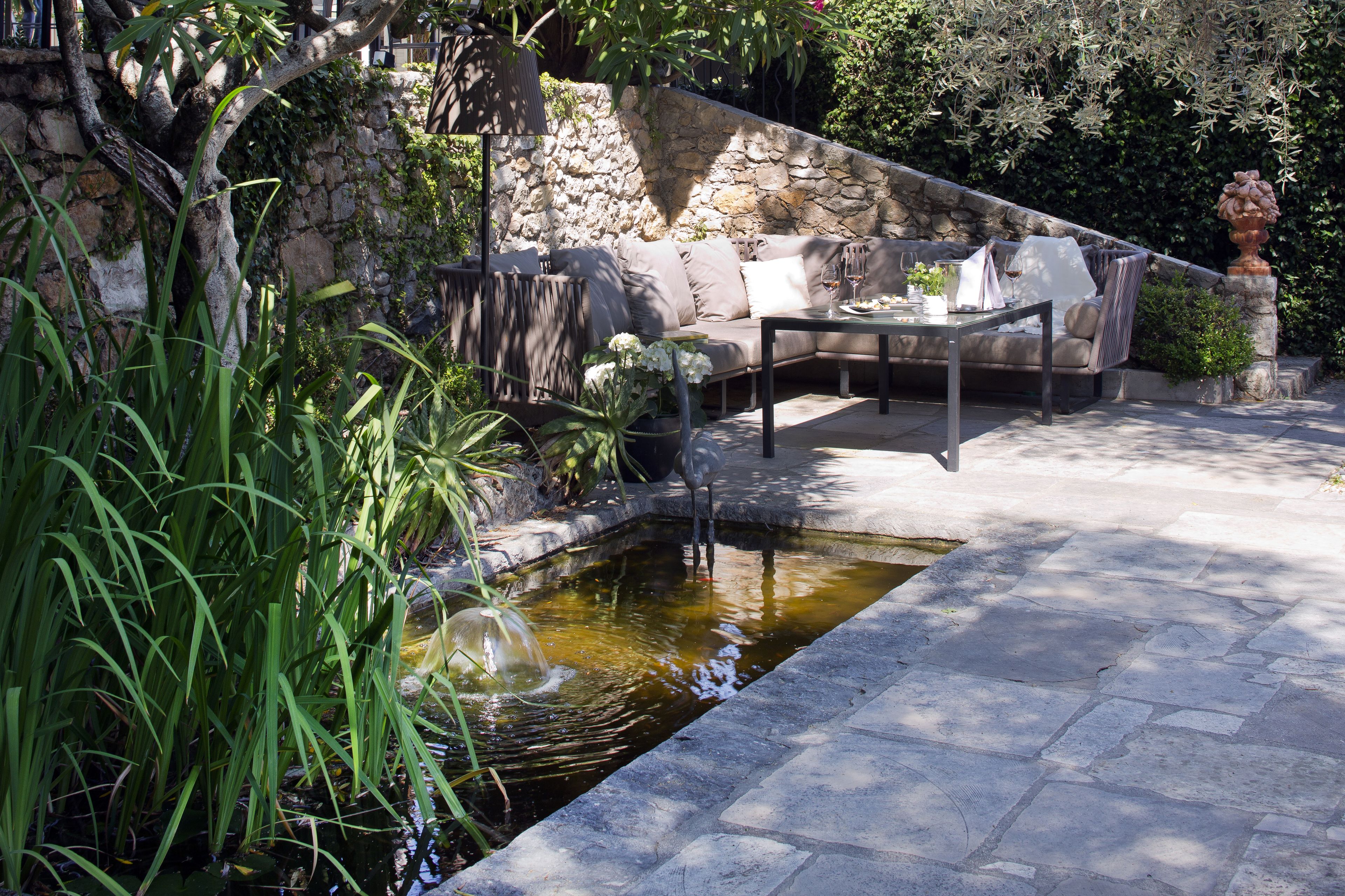 A stone wall, a stone bench, a small pond, and a dining table with chairs.