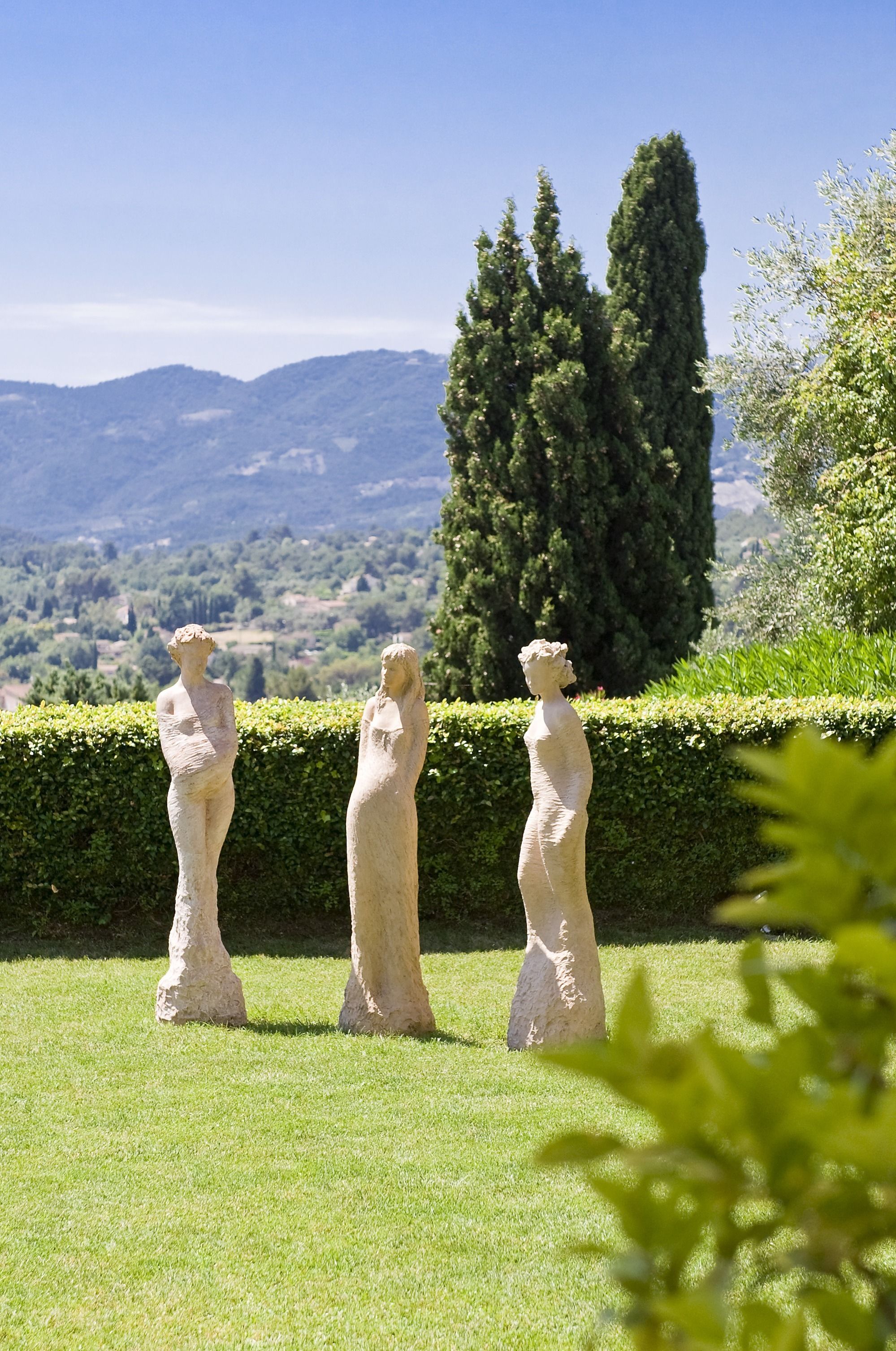 Trois statues de pierre dans un jardin, avec vue sur des montagnes lointaines.