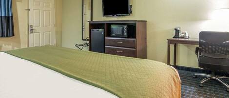 A hotel room with a bed, a desk with a computer, a television, and a microwave.