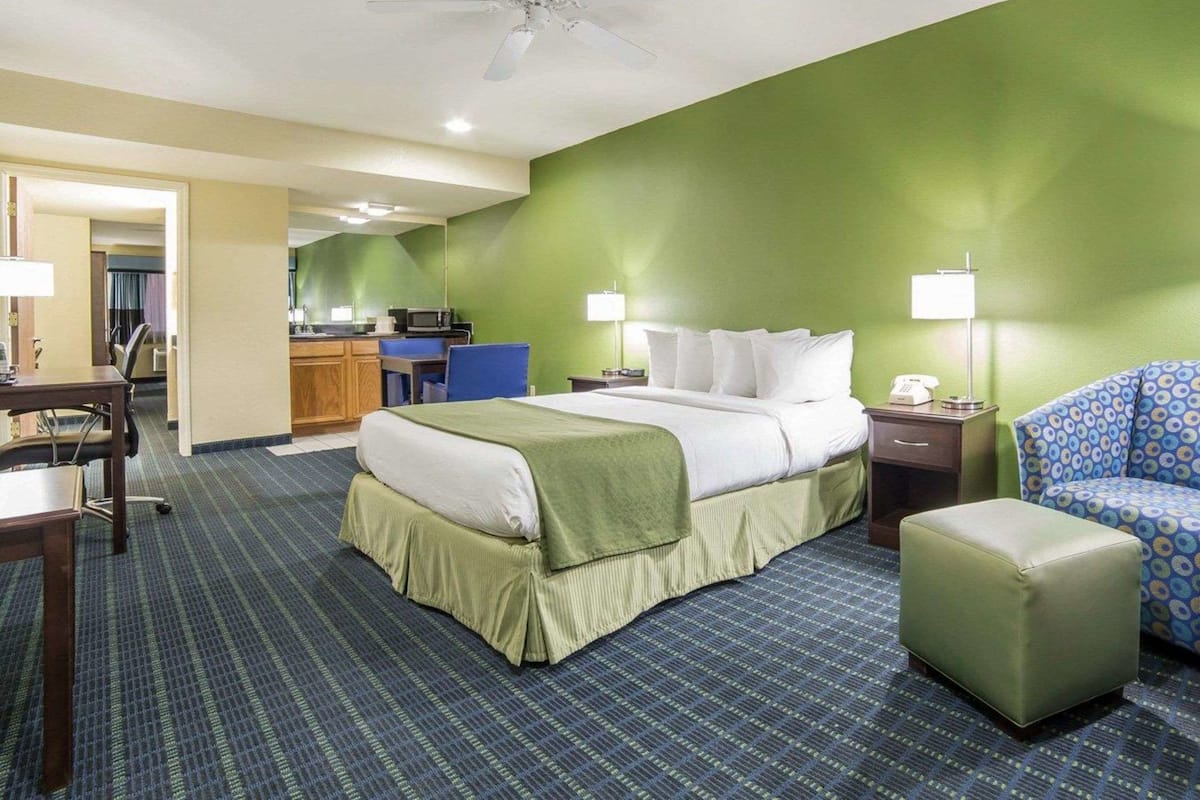 Quarto de hotel com cama, escrivaninha, cadeira, cozinha compacta e banheiro.