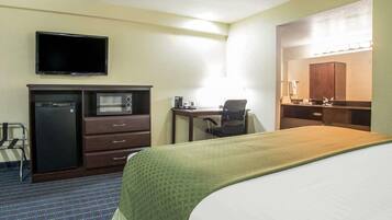 A hotel room with a bed, a desk with a chair, a television, a microwave, and a refrigerator.