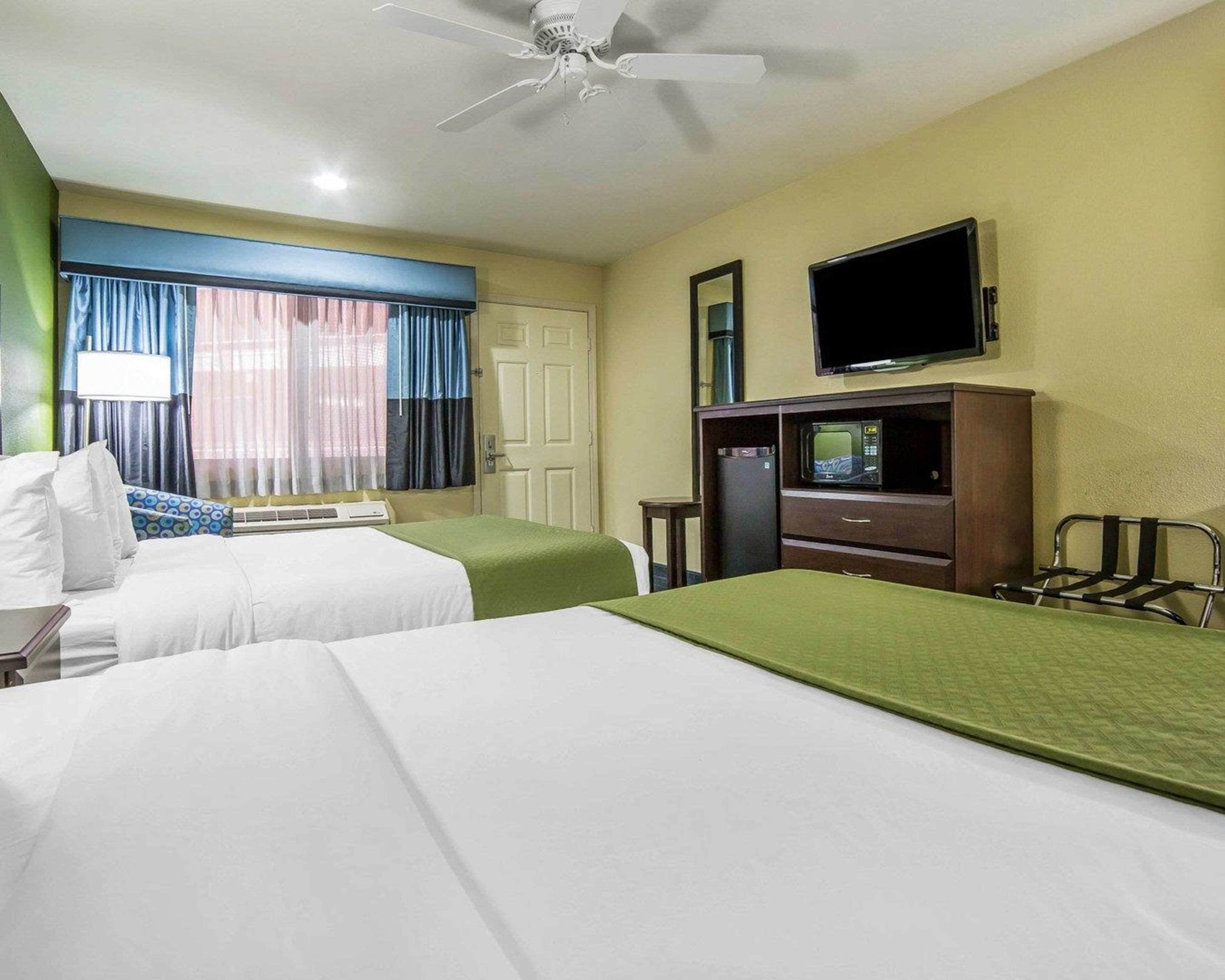 A hotel room with two beds, a television, a microwave, and a ceiling fan.