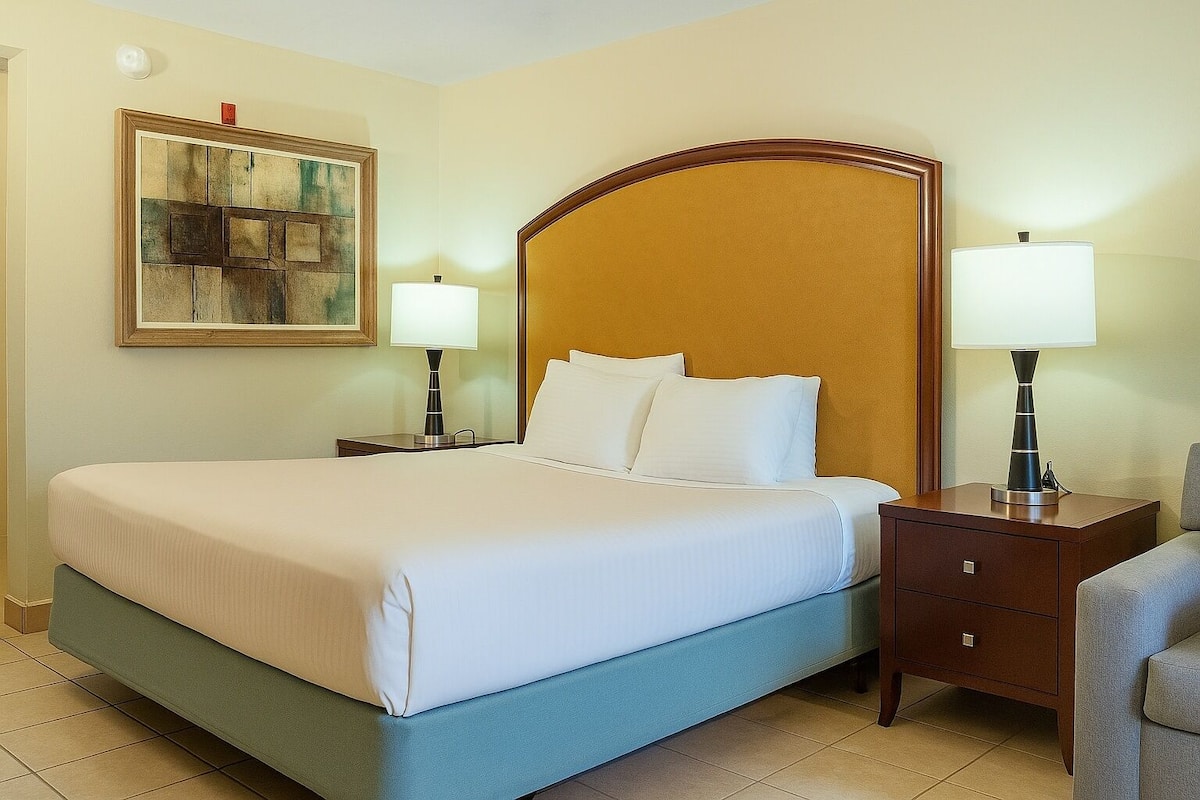 A hotel room with a large bed, two bedside tables with lamps, a wooden headboard, and a painting on the wall.