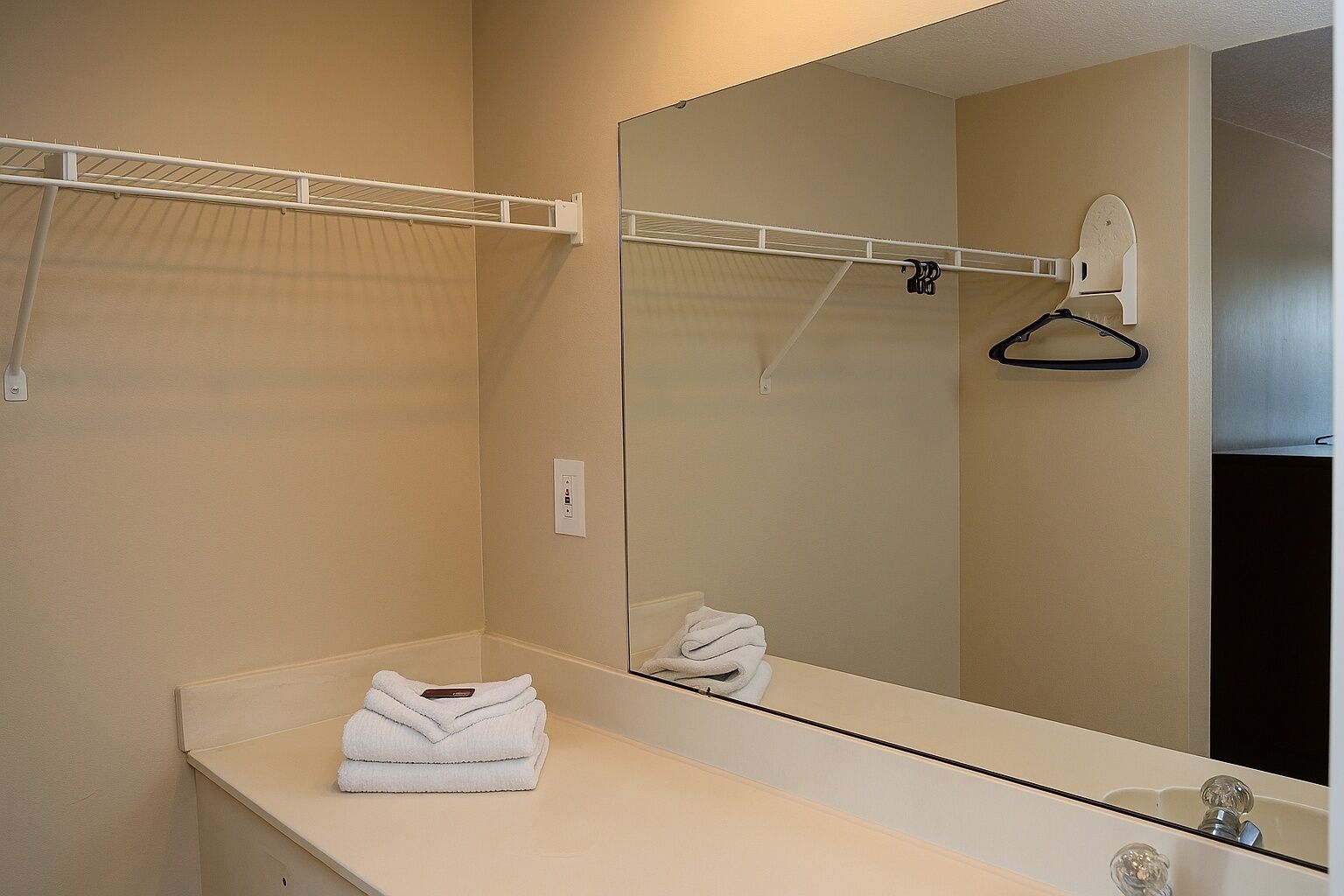 A bathroom with a white countertop, a mirror, a towel rack, and a hanging towel.