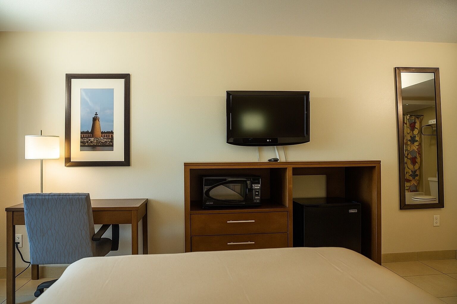 Une chambre d’hôtel équipée d’un lit, d’un bureau avec une lampe, d’une télévision, d’un four à micro-ondes et d’un réfrigérateur.