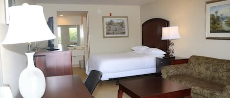 Una habitación de hotel con cama, escritorio, silla, sofá y televisor.