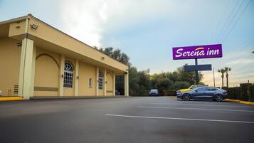 A hotel with a large sign reading "Serena Inn" and a parking lot with cars.