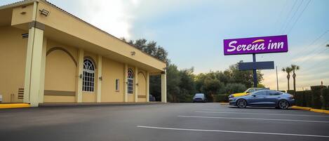 Un hotel con un letrero grande que dice "Serena Inn" y un estacionamiento con coches.