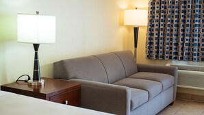 A hotel room with a bed, a bedside table with a lamp, a sofa, and a patterned curtain.