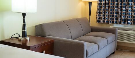 Habitación de hotel con una cama, una mesita de noche con lámpara, un sofá y una cortina estampada.
