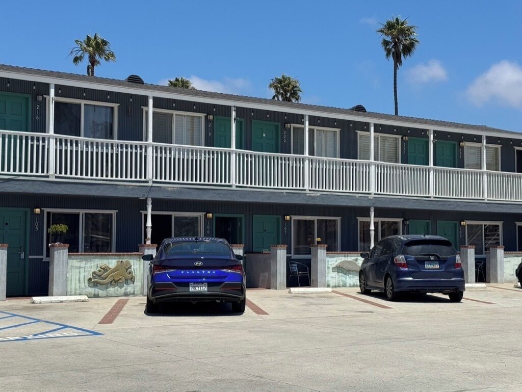 Ein Motel mit zweigeschossigen Gebäuden, einem Parkplatz und zwei parkenden Autos davor.