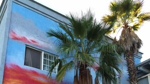 A mural of a red car on a beach with palm trees and a sunset. - The Shores Inn and Beach Houses (Ventura)