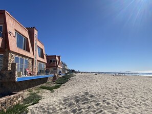 A beachfront hotel with stone and stucco exteriors, large windows, and a blue railing along the beach. - The Shores Inn and Beach Houses (Ventura)