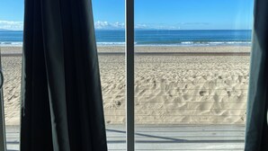 A beach view through a window with curtains, sandy beach, and ocean. - The Shores Inn and Beach Houses (Ventura)