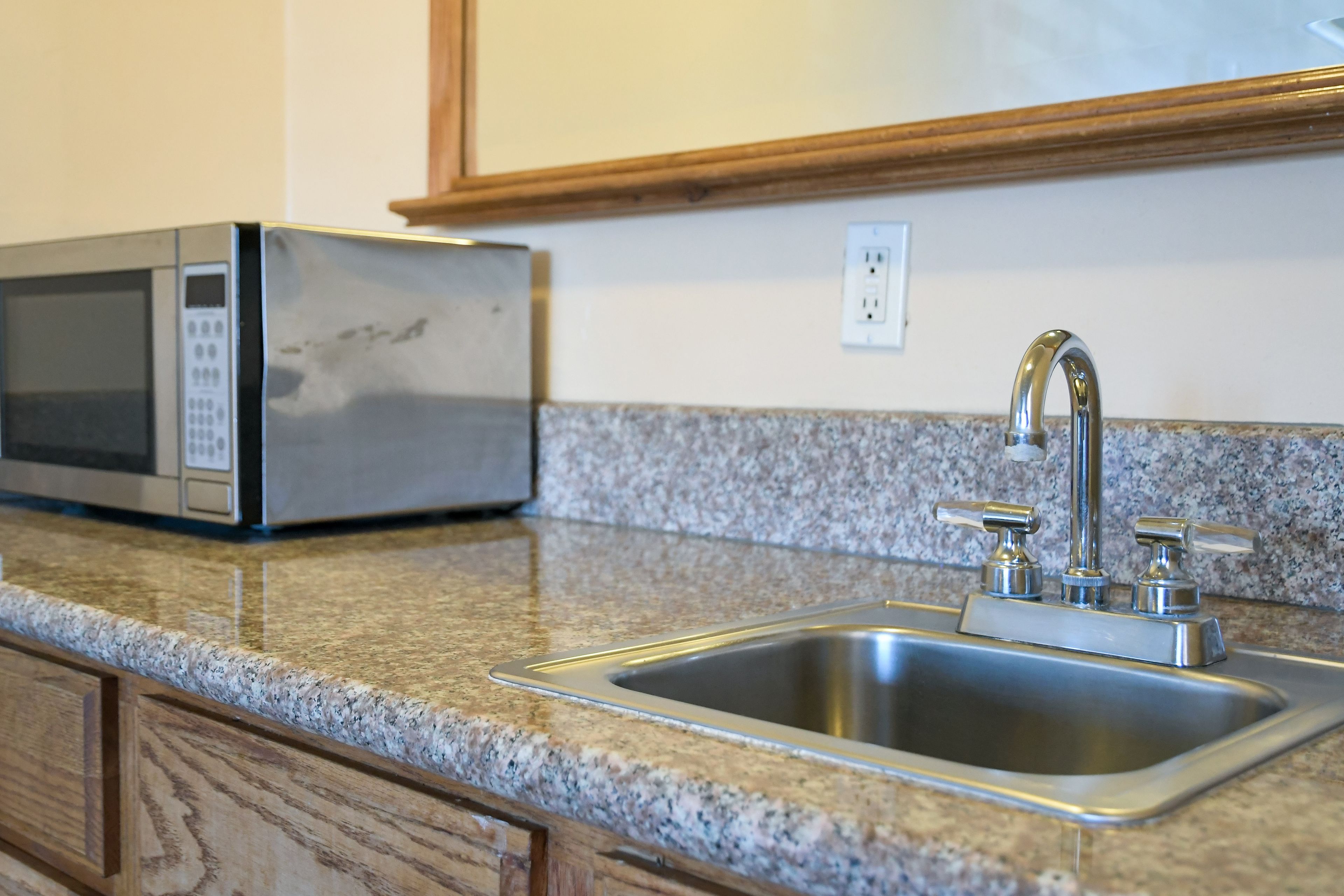 A kitchen with a stainless steel sink, granite countertop, and a microwave.