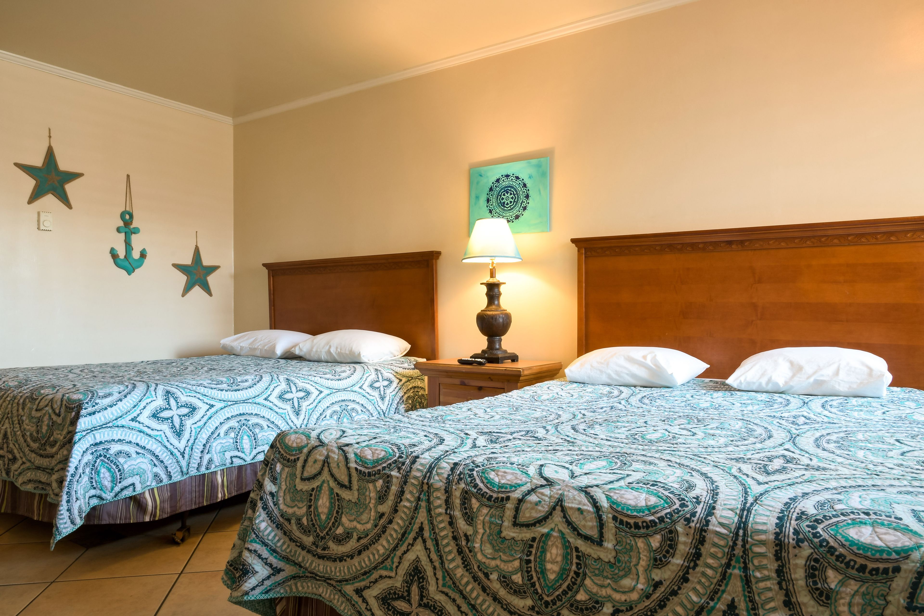 Habitación de hotel con dos camas, una mesita de noche con lámpara y adornos en la pared que incluyen estrellas y un diseño circular.