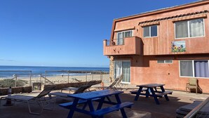 A building with a balcony overlooking a beach, featuring outdoor seating and a view of the ocean. - The Shores Inn and Beach Houses (Ventura)