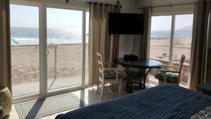 A room with a bed, a TV, a table, and chairs, overlooking a beach. - The Shores Inn and Beach Houses (Ventura)