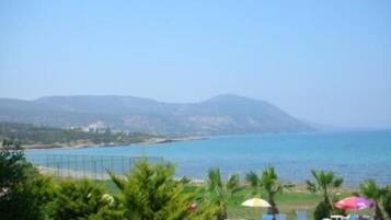 Zona junto a la piscina con sillas de descanso y sombrillas, con vistas a un paisaje costero y montañas al fondo.