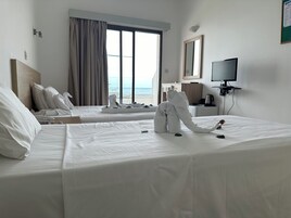 Una habitación de hotel con dos camas, televisión, escritorio y vista al mar.