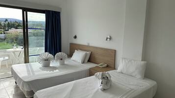 Quarto de hotel com duas camas, varanda com mesa e cadeiras, e vista da paisagem circundante.