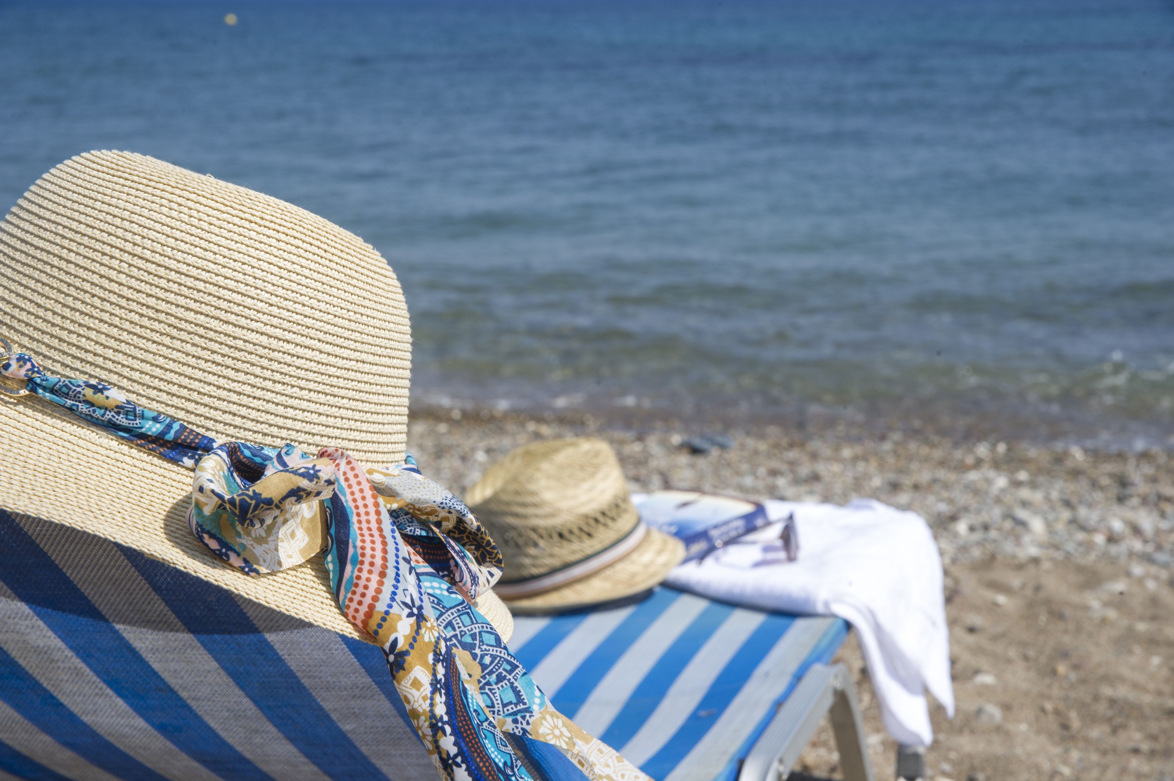 A beach scene with a straw hat and a striped towel on a lounge chair.