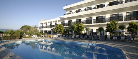 A modern hotel with a swimming pool, lounge chairs, and a clear view of the mountains.