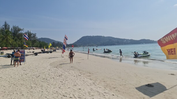 A beach with flags, a jet ski, and a signboard. - Pipikuku Hotel & Restaurant (Patong)