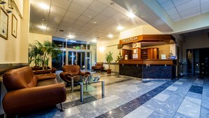 A hotel reception area with leather sofas, a reception desk, and potted plants. - Olymp Spa (Kolobrzeg)