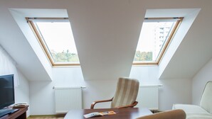 A room with a sloped ceiling, two skylights, a wooden table, a chair, a sofa, a TV, and a radiator. - Olymp Spa (Kolobrzeg)