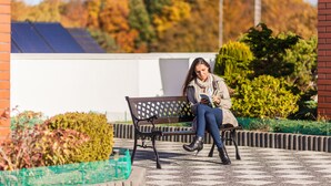 A woman sitting on a bench in an outdoor area with a patterned floor, surrounded by greenery and a building with a solar panel roof. - Olymp Spa (Kolobrzeg)