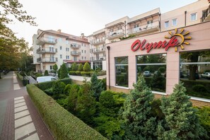 Een hotel met een zonlogo, meerdere balkons en een verzorgde tuin.