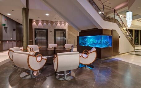 A lobby with a reception desk, two elevators, a large aquarium, and seating area with modern chairs.