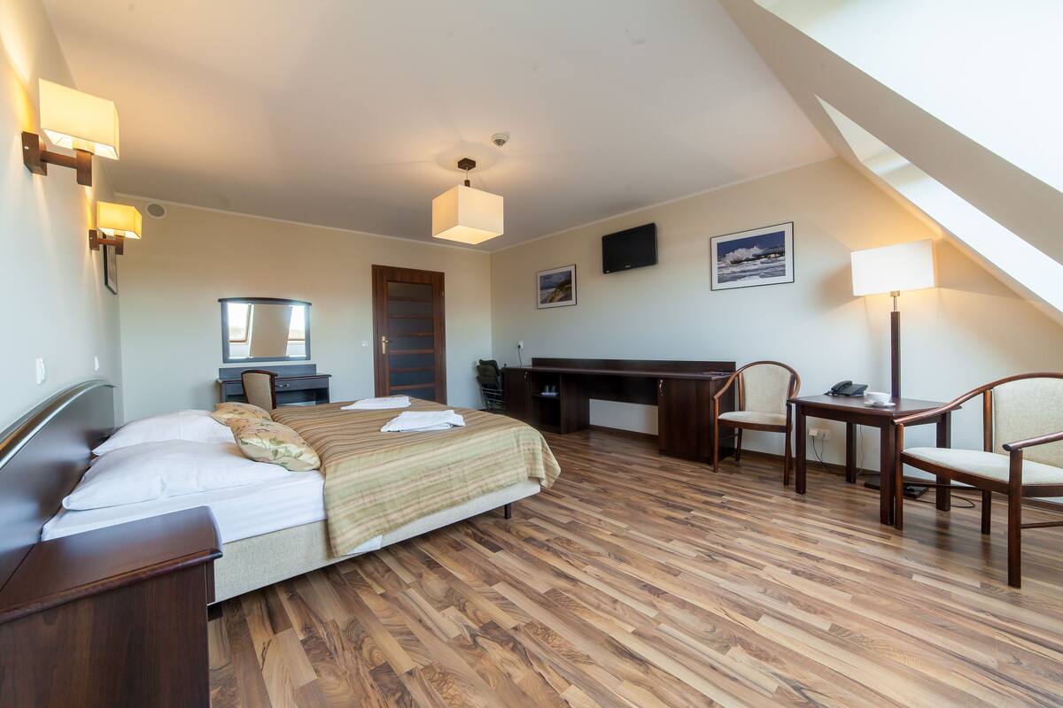 A hotel room with a bed, desk, chairs, and a TV.