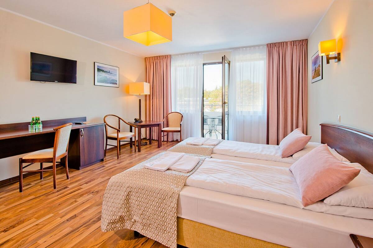 A hotel room with a bed, desk, chairs, and a TV.