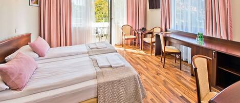 A hotel room with a large bed, a desk, and a chair. There is a window with curtains, a television, and a lamp.