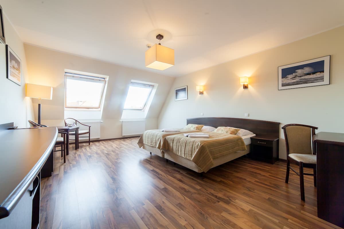 A bedroom with a bed, two bedside tables, a desk, a chair, and two windows.