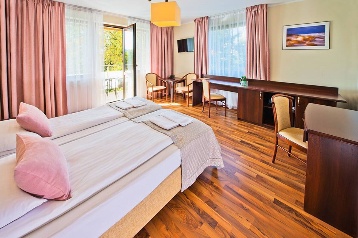 A hotel room with a large bed, a desk, and a chair. There is a balcony with a table and chairs.