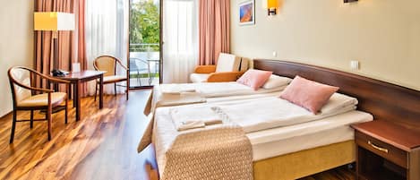 A hotel room with two beds, a desk, chairs, a small table, and a balcony with curtains.