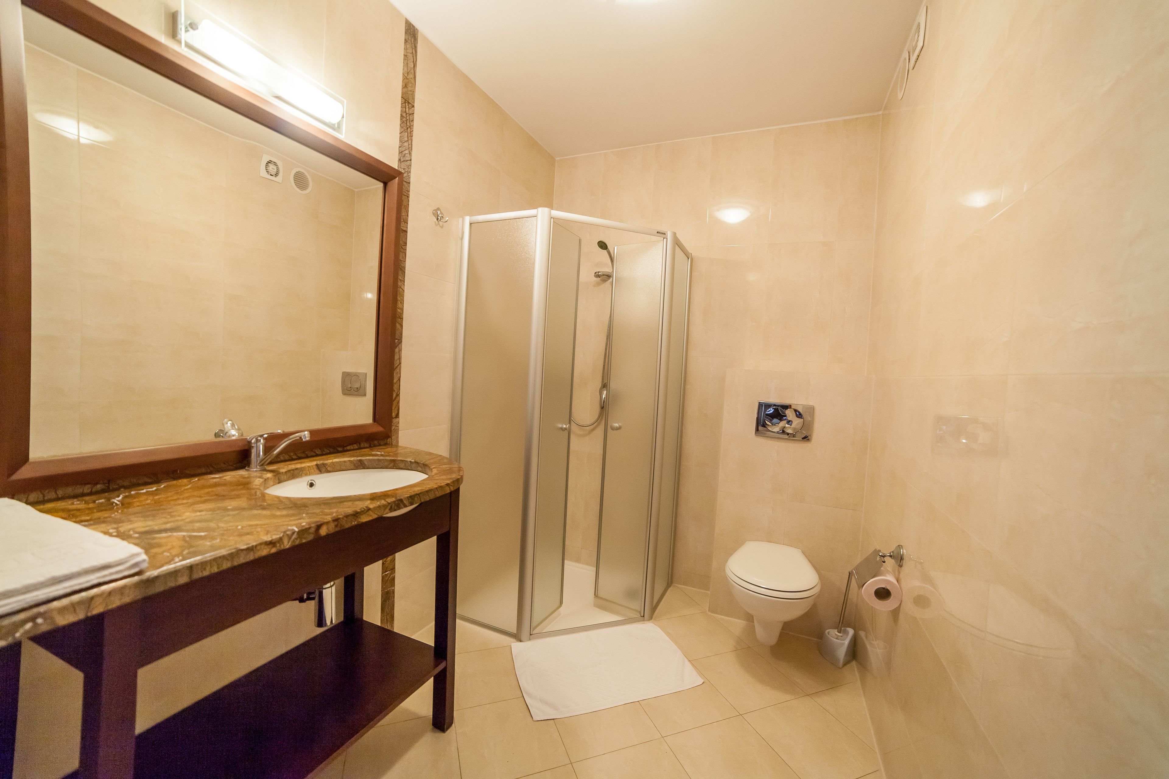 A bathroom with a glass-enclosed shower, a sink with a marble countertop, and a toilet with a paper towel dispenser.