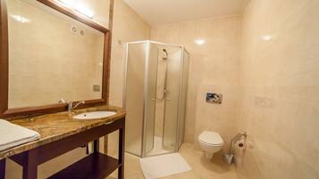 A bathroom with a glass-enclosed shower, a sink with a marble countertop, and a toilet with a paper towel dispenser.