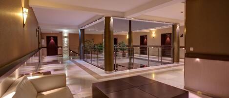 A spacious lobby with a modern design, featuring a seating area, a glass railing, and a central column.