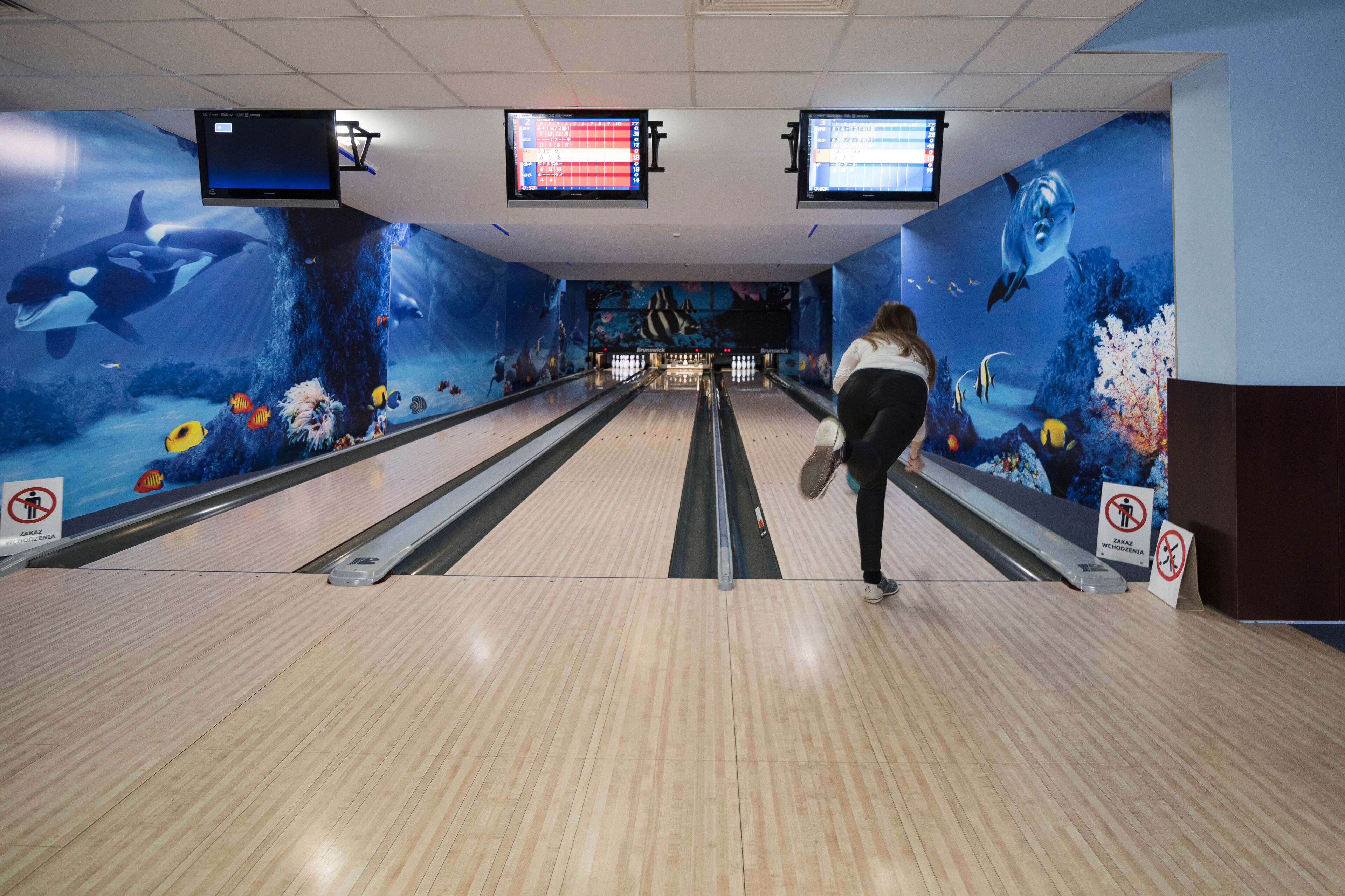 A bowling alley with a marine-themed mural on the walls and overhead scoreboards.
