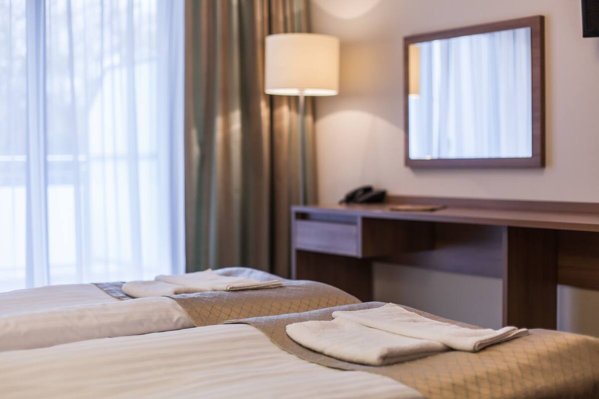 Ein Hotelzimmer mit zwei Betten, einem Schreibtisch, einer Lampe und einem Spiegel.