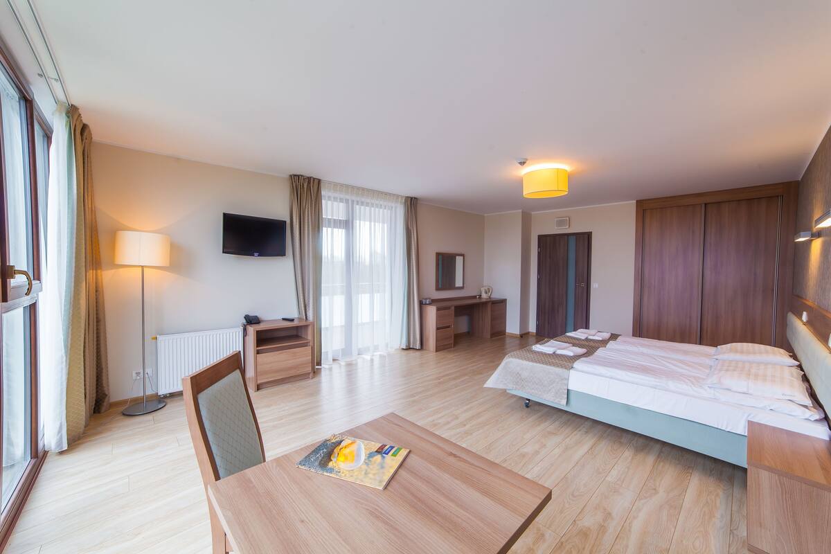 Ein Hotelzimmer mit Bett, Schreibtisch, Stuhl, Lampe, Fernseher und Blick ins Freie.